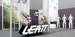 CAD-Visualisierung: Nahansicht eines Messestands für die Firma Leatt in Weiß und Grau. Ein durchscheinender Vorhang aus dünnen Stäben gibt den Blick auf ein Foto grüner Berglandschaft und das LEATT-Logo frei. Auf einem Podest stehen drei Helme auf Ständern, einer silbern, einer mit rotem Farbspritzer und einer orangefarben, davor das schwarz-weiße LEATT-Blocklogo. Rechts mehrere weiße Schaufensterfiguren und ein weißer Würfel. CAD-Visualisierung erstellt von Torsten Kraus.