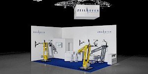CAD-Visualisierung: Perspektivische Ansicht eines Messestands für die Firma Zeilhofer Handhabungstechnik in Weiß mit blauem Teppichboden vor dunklem Hintergrund. An einer Traverse mit Scheinwerfern hängt ein weißer Würfel mit dem ZEILHOFER-Logo. Die weißen Wände zeigen das Logo und schwarze Grafiken von Roboterarmen sowie ein gerahmtes Bild. Zwei große gelbe Industrie-Roboterarme stehen auf Sockeln und werfen deutlich sichtbare Schatten an die weißen Wände; dazwischen eine weiße Theke mit schwarzen Barhockern. CAD-Visualisierung erstellt von Torsten Kraus.
